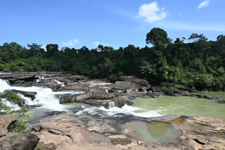 Waterfall cascades over smooth brown boulders into the green river.
