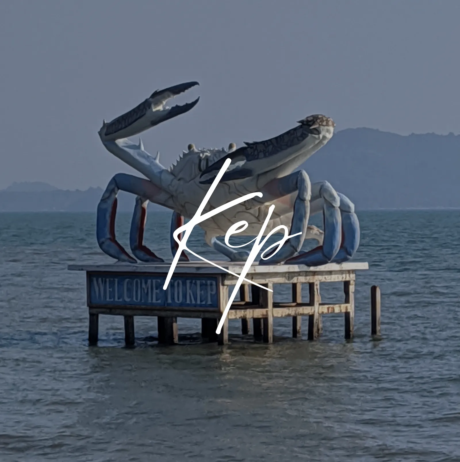 A large sculpture of a crab sits on a platform in the ocean at Kep in Cambodia. Text overlay reads Kep.