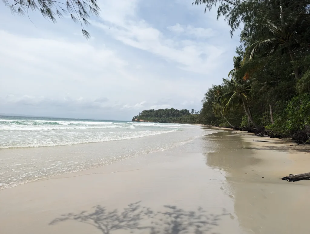 Quiet sandy shoreline at Lonely Beach on Koh Rong, Cambodia, with calm water and tropical trees.