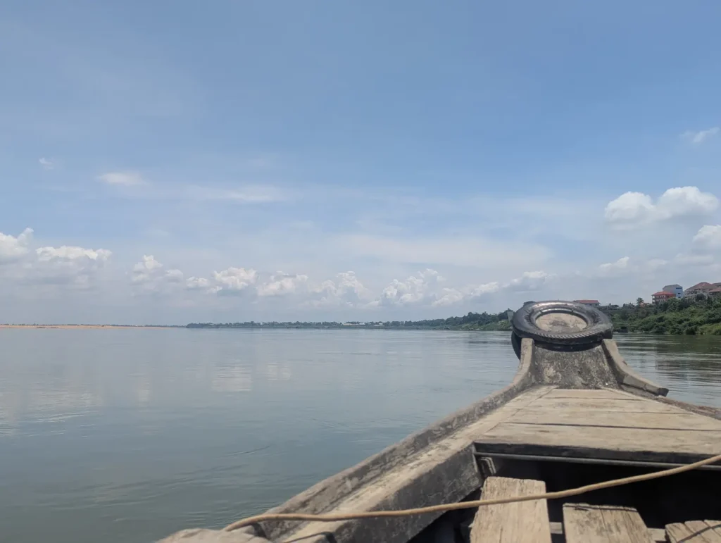 A traditional wooden boat rests on the right side of the Mekong River in Kratie, Cambodia, with calm waters reflecting the soft morning light.