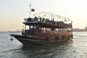 A wooden boat with two levels on the river. People are having a party on the top.