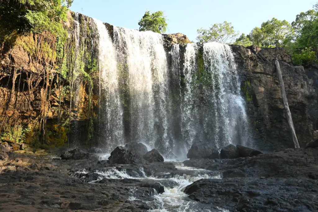 A close up of a waterfall approximately 8 metres high. The sun shines across half of the waterfall.