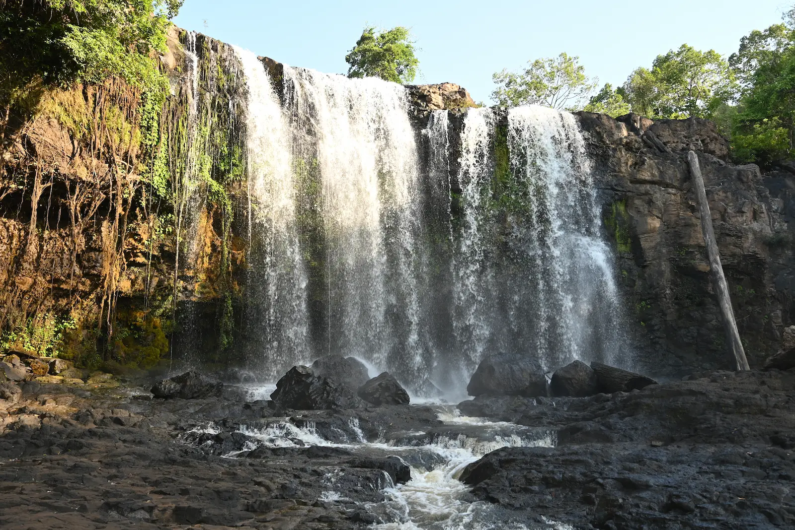 A close up of a waterfall approximately 8 metres high. The sun shines across half of the waterfall.