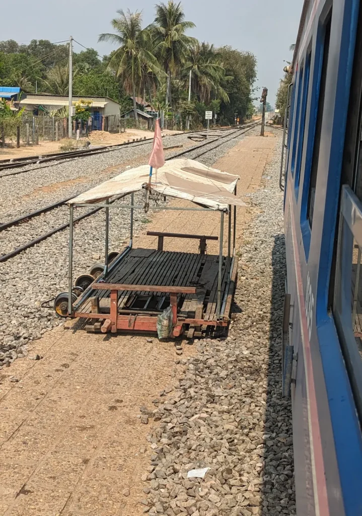 A large passenger train is next to a small bamboo train with a cover over it.