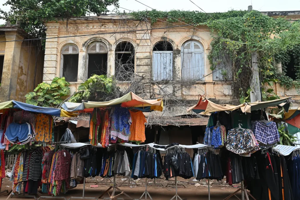 A market stall with umbrellas sits before old buildings with trees growing in them.