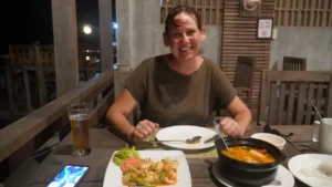 Mel is smiling. In front of her is two dishes, one of prawns and the other of soup.