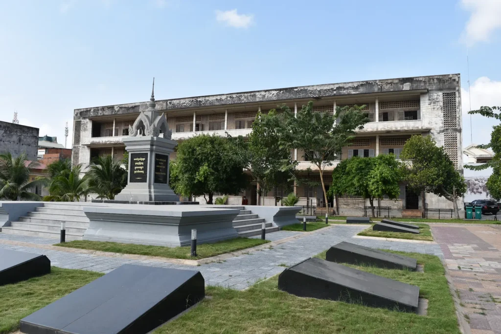 A new grey memorial is in the centre of the courtyard with an old school building in the background.