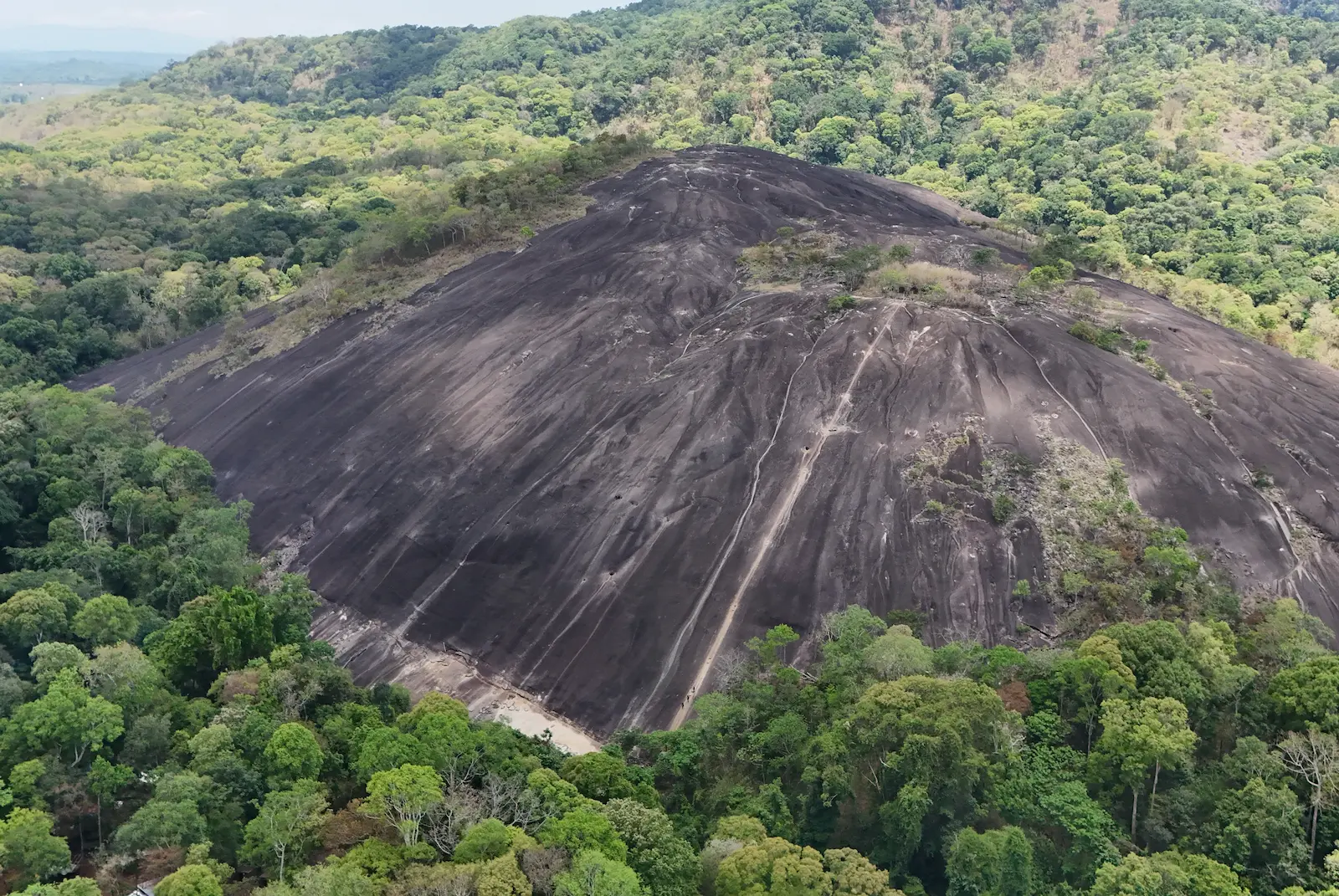 Drone shot of Nam Lear with large rock face and forest all around.
