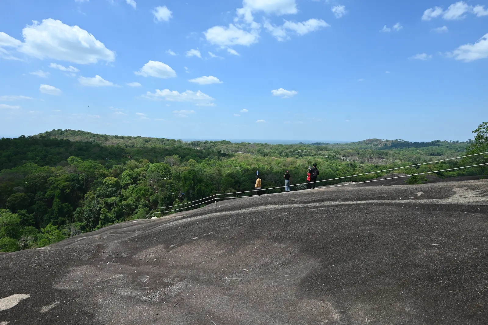 The large rock of Nam Lear is in the foreground, and in the middle you can see people climbing it. In the background is the forest.