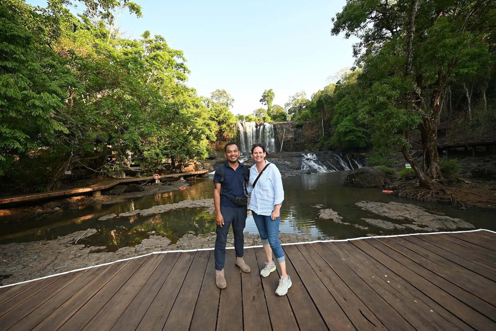 Nehru and Mel stand on a boardwalk in front of Bousra Waterfall