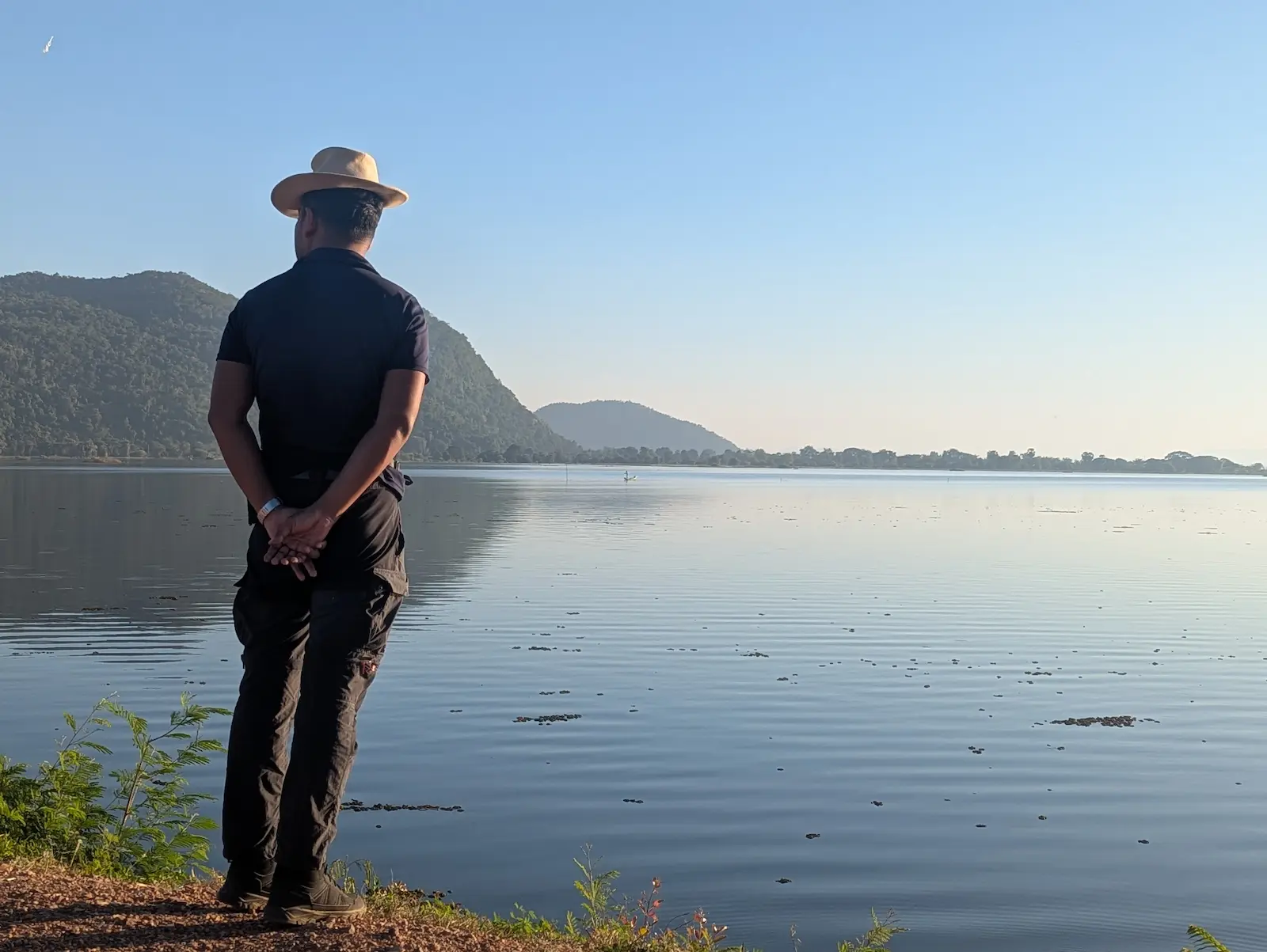 Nehru stands near a reservoir. He is wearing a hat and looking off into the distance.