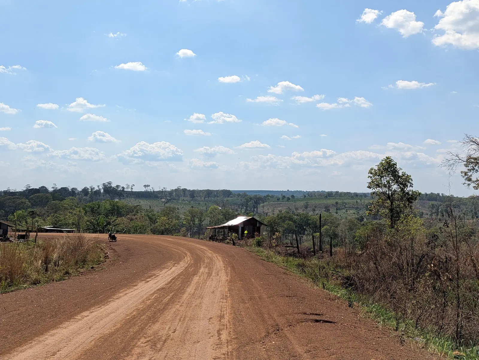 A red road runs to the left. Straight ahead is a house with the Mondulkiri landscape in the background.
