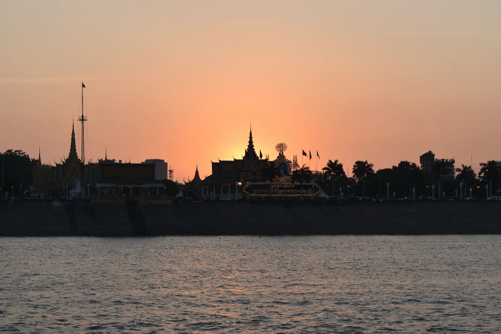 The sun sets behind the royal palace making the sky orange. In front is the river.