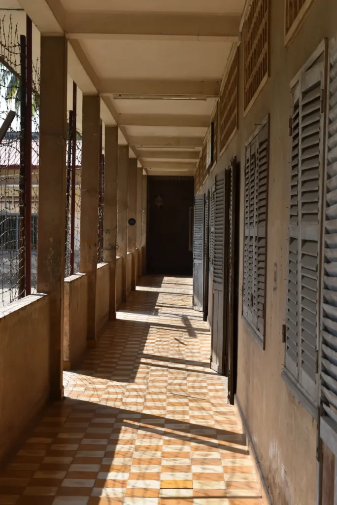A long corridor on the second floor has rooms and windows on one side, the other is covered in barbed wire.