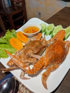 Two cooked crabs sit on a plate with some chilli sauce.