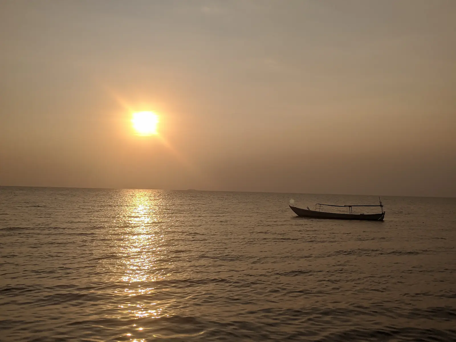 The sun sets over one fishing boat which sits to the right of the photo in the water.