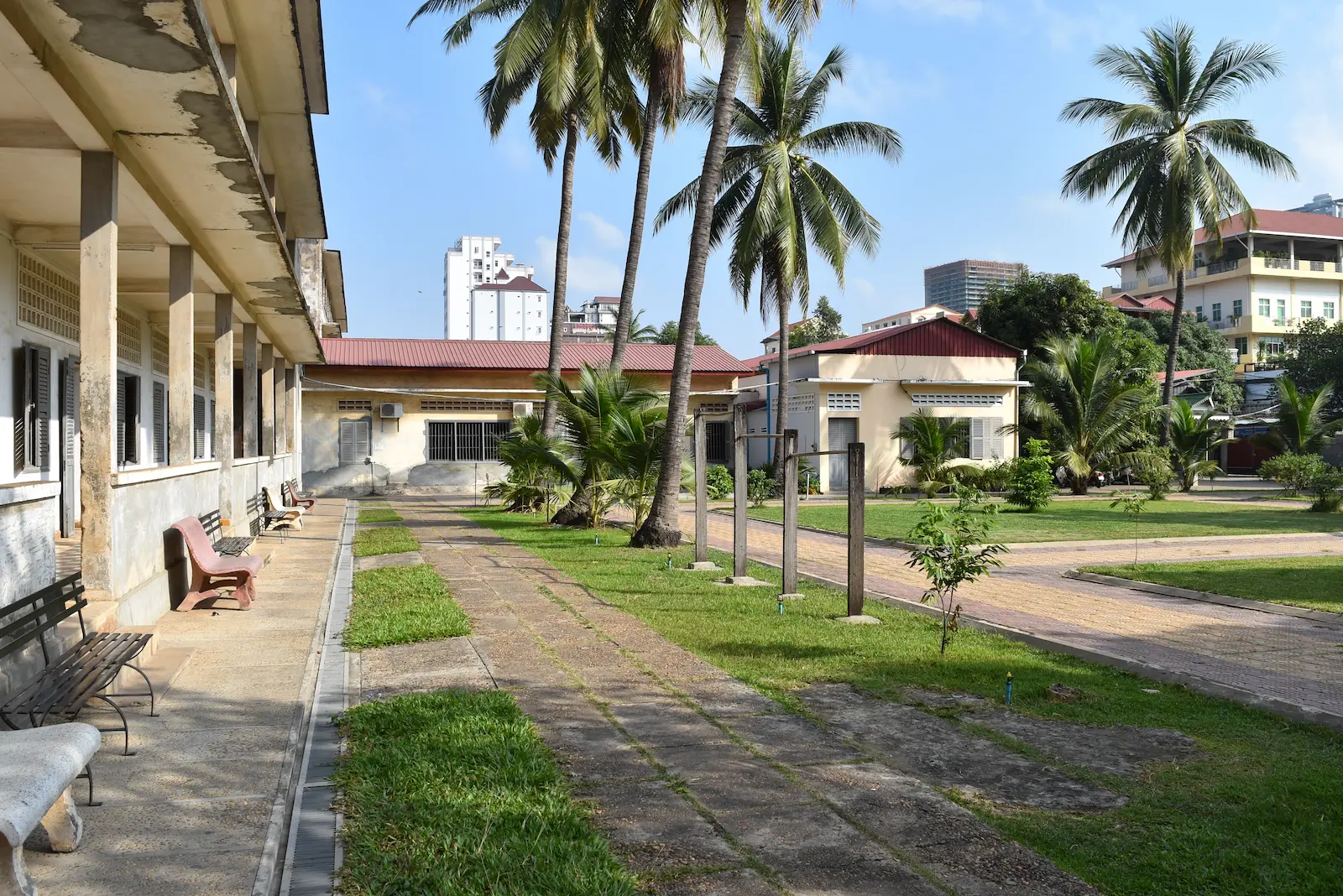A school building with green grass and palm trees at Tuol Sleng S21 prison