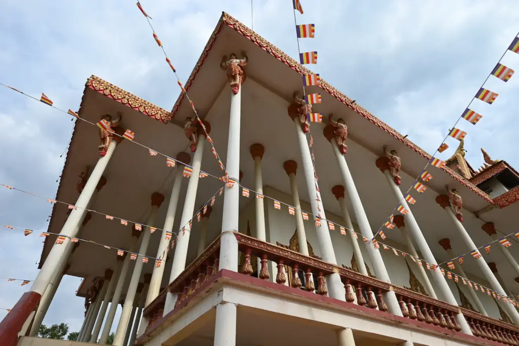 Photo of a pagoda with many columns. Buddhist flag bunting plies in front of the pagoda.