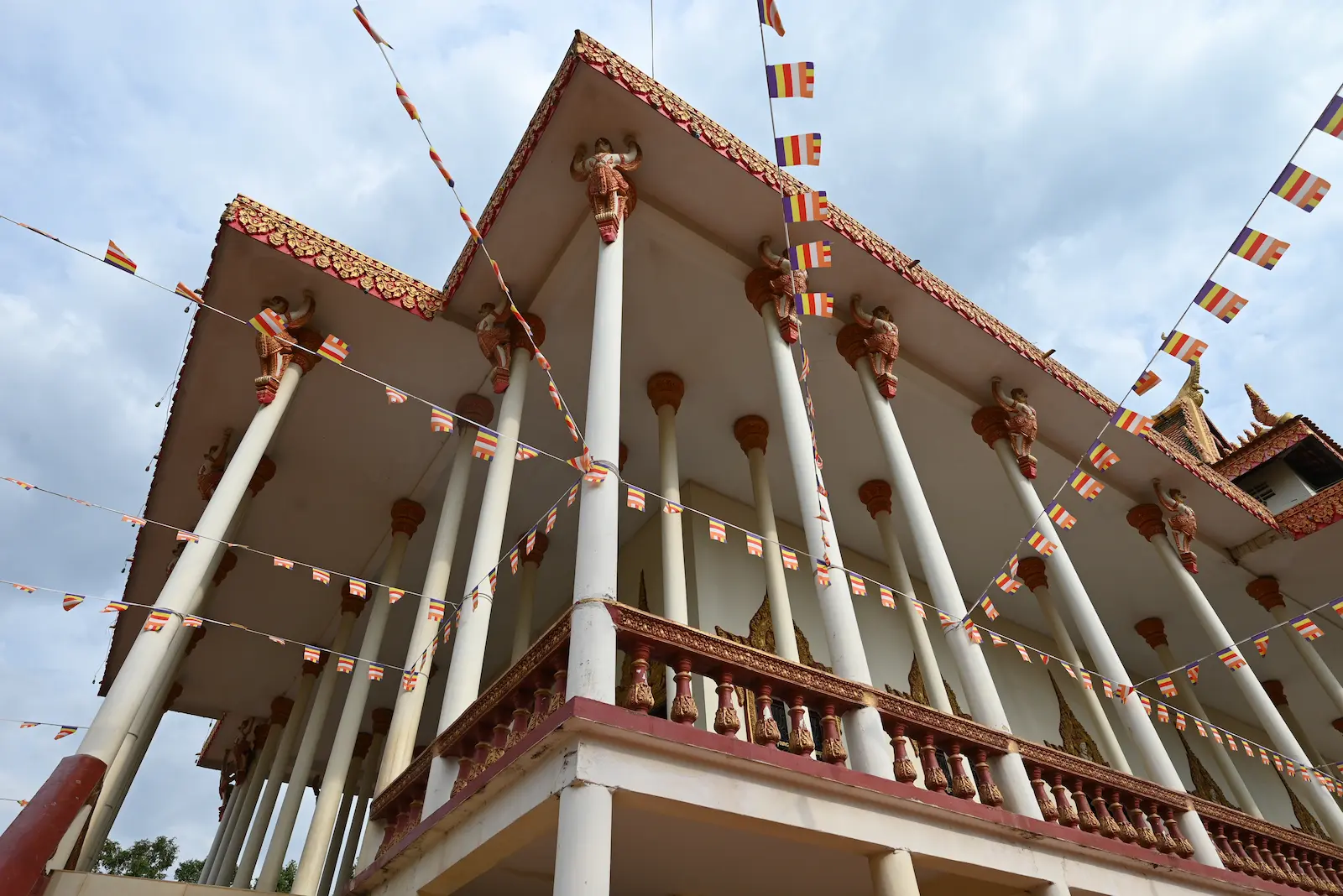 Photo of a pagoda with many columns. Buddhist flag bunting plies in front of the pagoda.