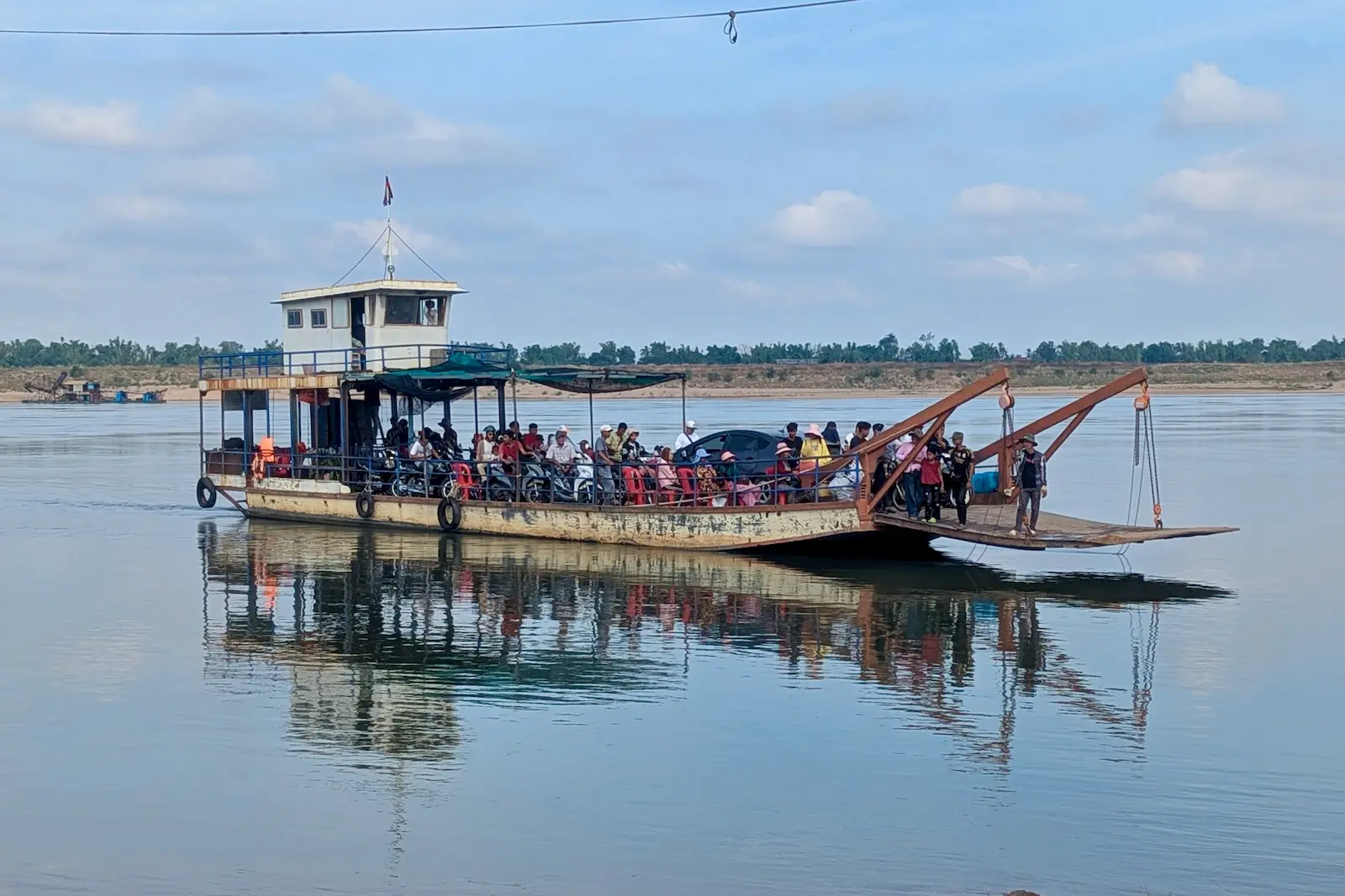 A ferry filled with cars, motorbikes and people crosses the Mekong River