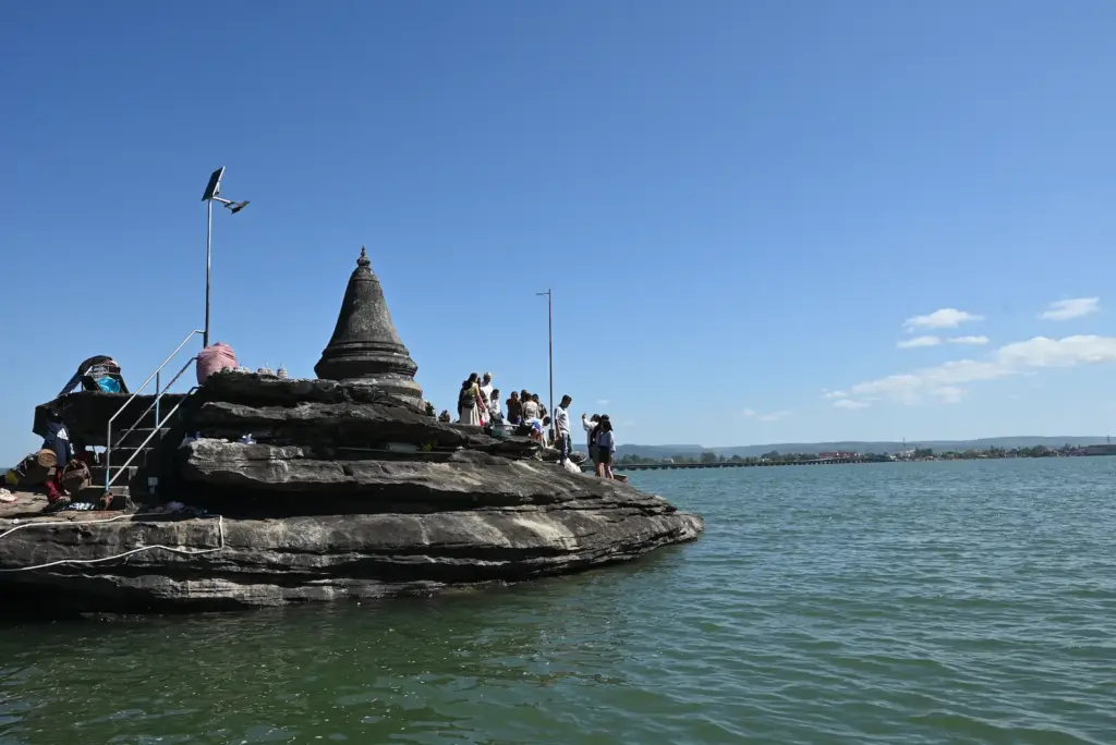A small stupa sits on some rocks in the Koh Kong river. Attached to it is a walking bridge.