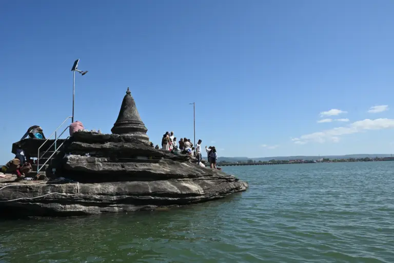 A small stupa sits on some rocks in the Koh Kong river. Attached to it is a walking bridge.