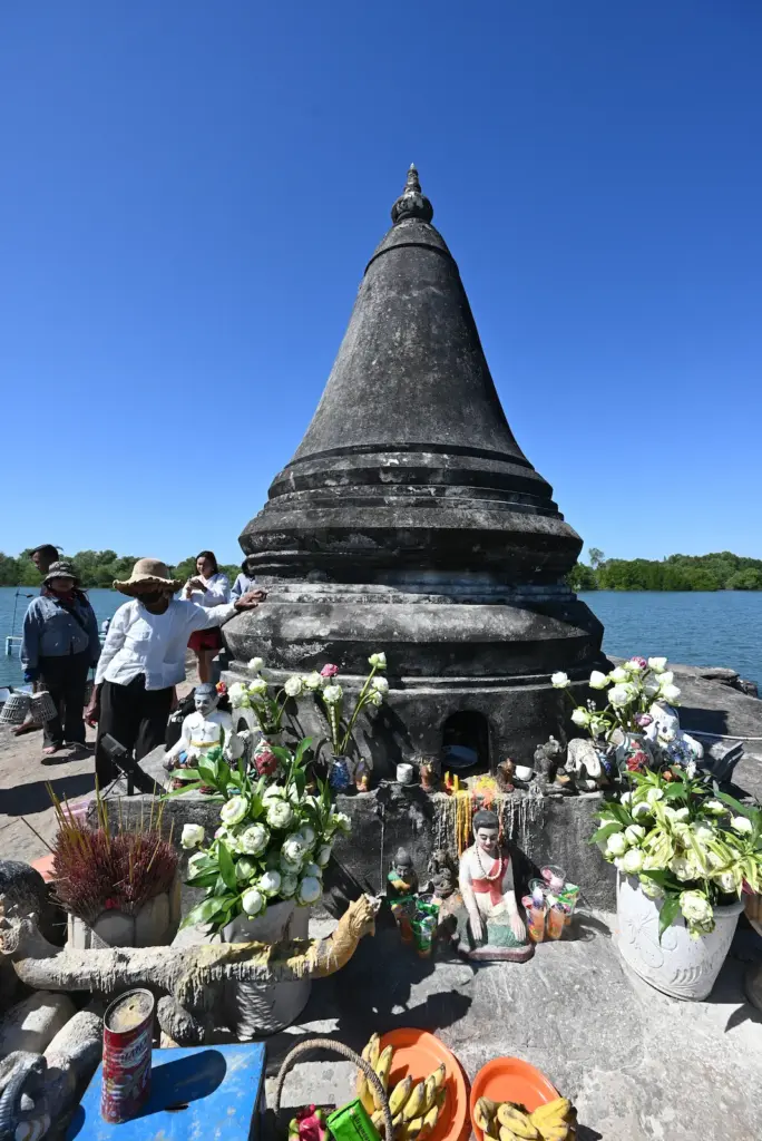 A stupa next to a river with flowers and offerings laid around it