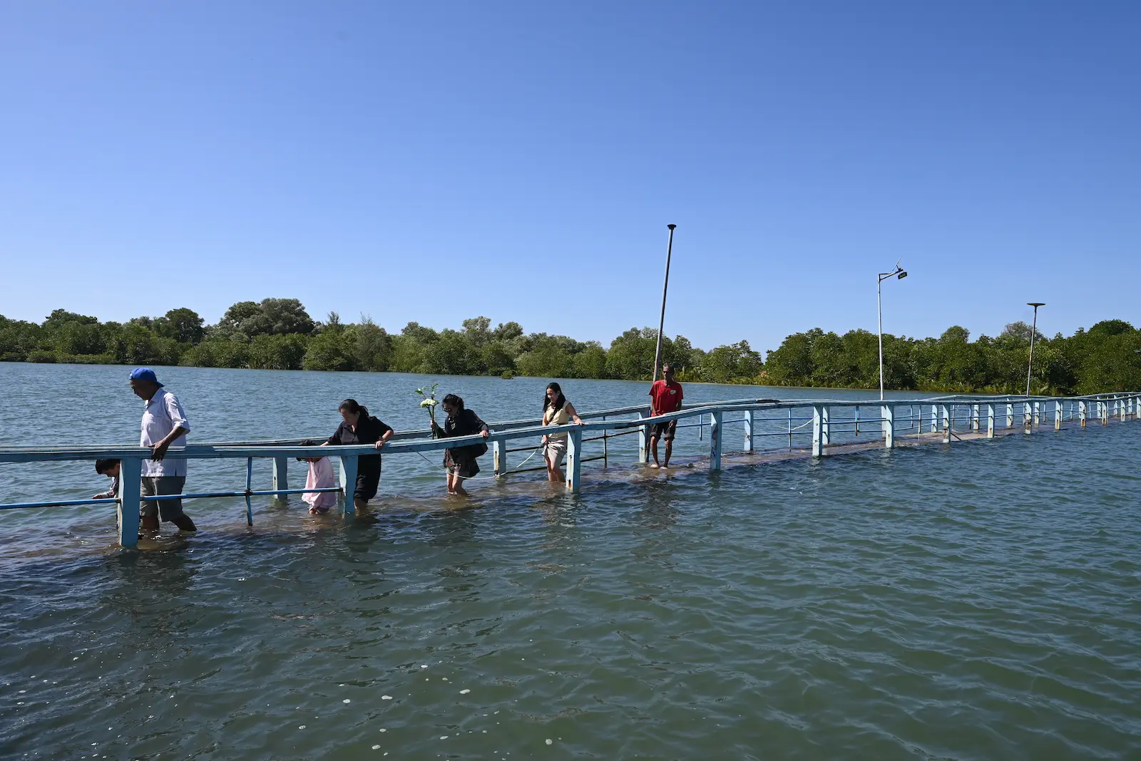 A group of people wade across a small causeway covered in water.