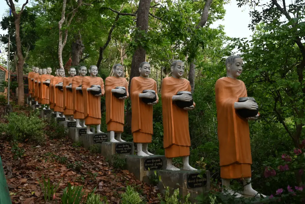 A line of monks sculptures holding alms jars are in a line coming down a hill.