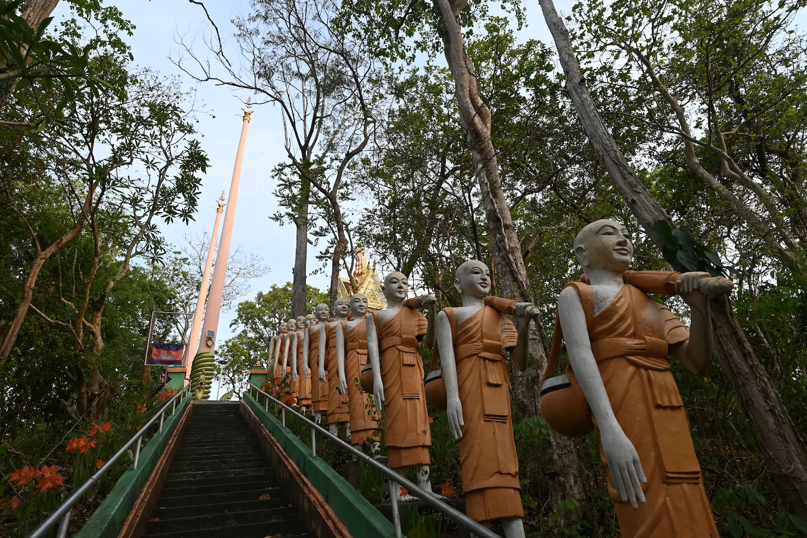 Statues of monks carrying umbrellas on their shoulders line the stairs to a shrine.