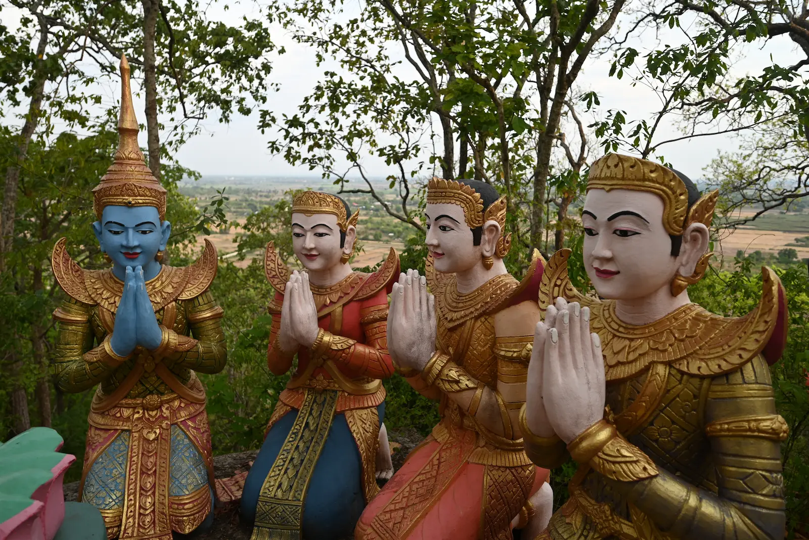 Statue of four celestial figures doing sampeau. In the background is green fields.