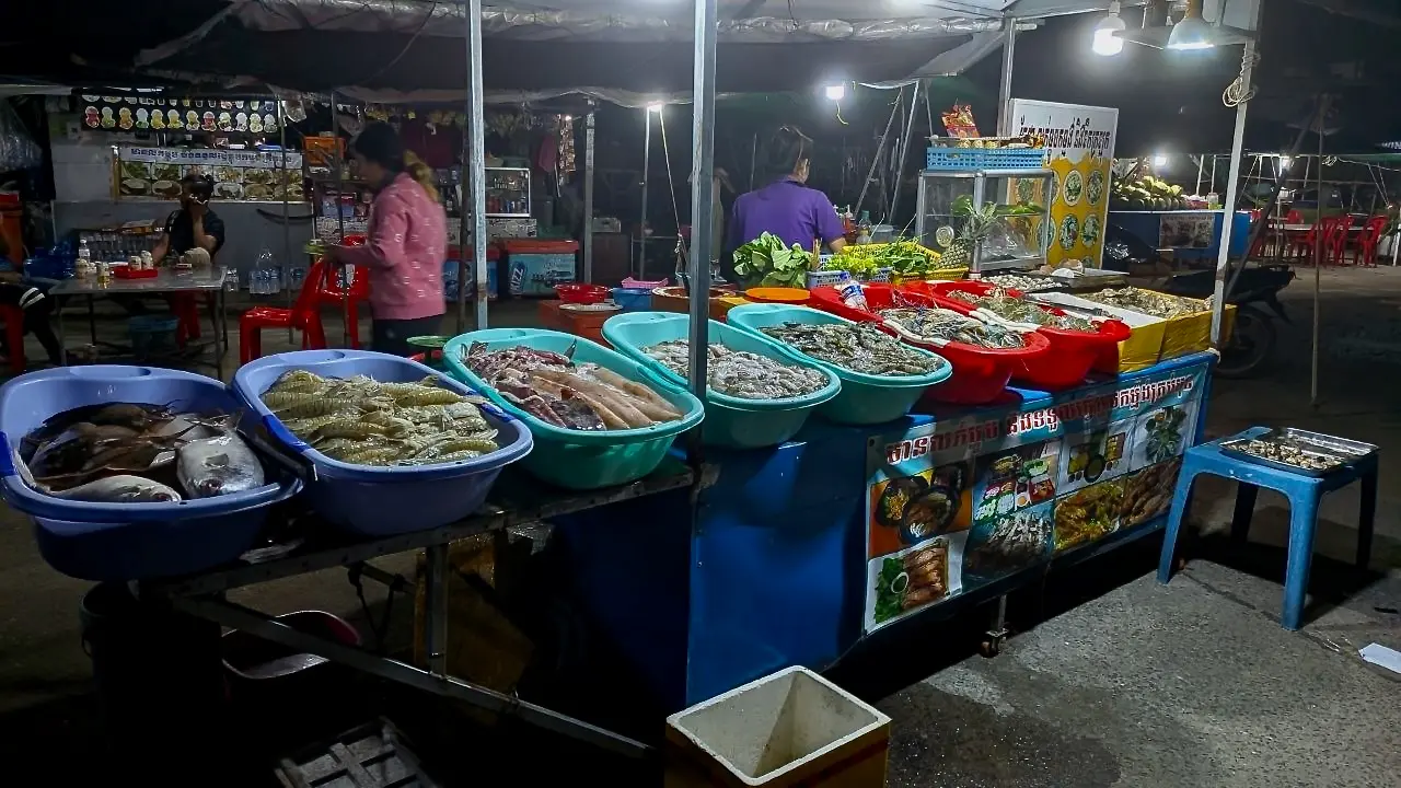 A temporary tent with colourful tubs full of different seafood at night.
