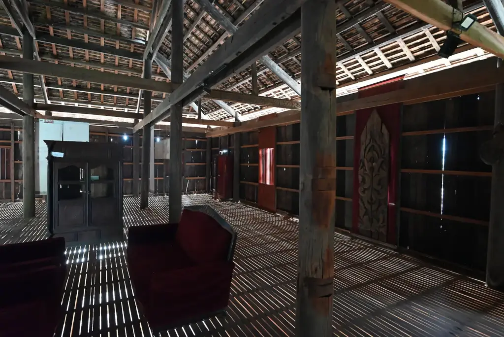 photos shows the corner of the old wooden house. You can see the light coming through the thin floorboards and three large pillars.