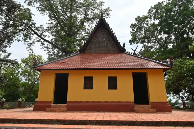 A yellow wooden temple with red roof tiles and a wooden carved pediment.