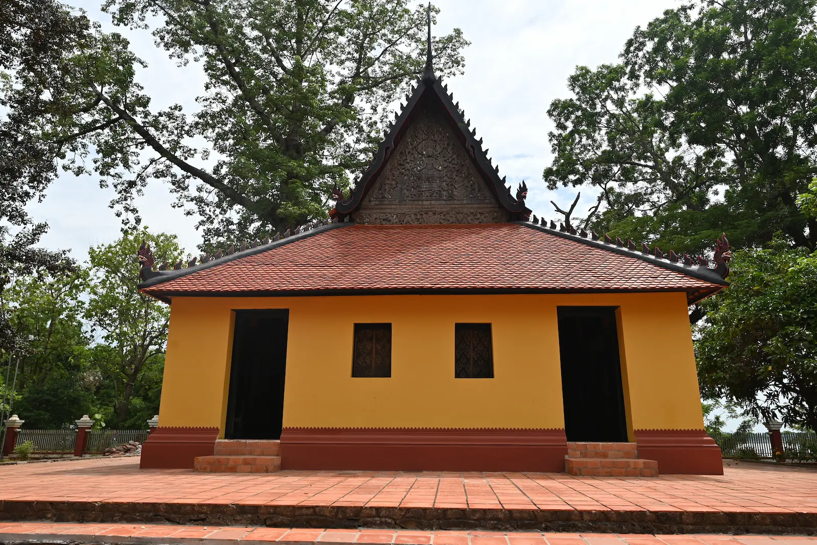 A yellow wooden temple with red roof tiles and a wooden carved pediment.