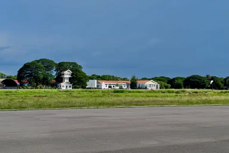 The Battambang airport terminal buildings and a tower with dark clouds behind it.