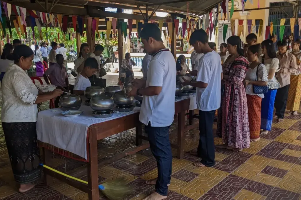 A line of people are putting rice into alms bowls in front of a pagoda.