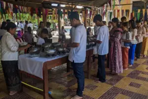A line of people are putting rice into alms bowls in front of a pagoda.
