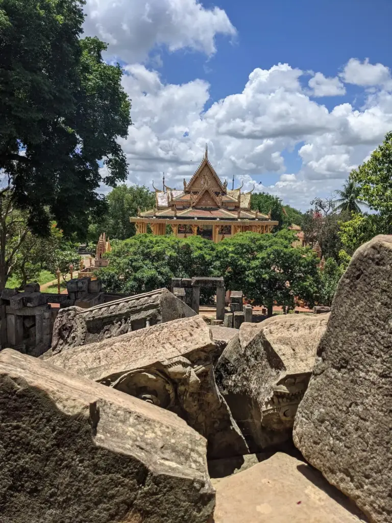 Fallen sandstone blocks and ruins of the ancient Ek Phnom Temple in Battambang, with the colourful modern Buddhist pagoda standing behind them.