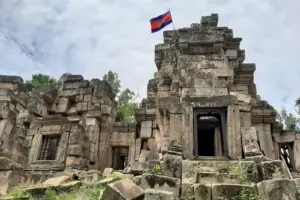 Ruins of the 11th-century Ek Phnom Temple in Battambang, with partially collapsed sandstone towers and large fallen stone blocks.