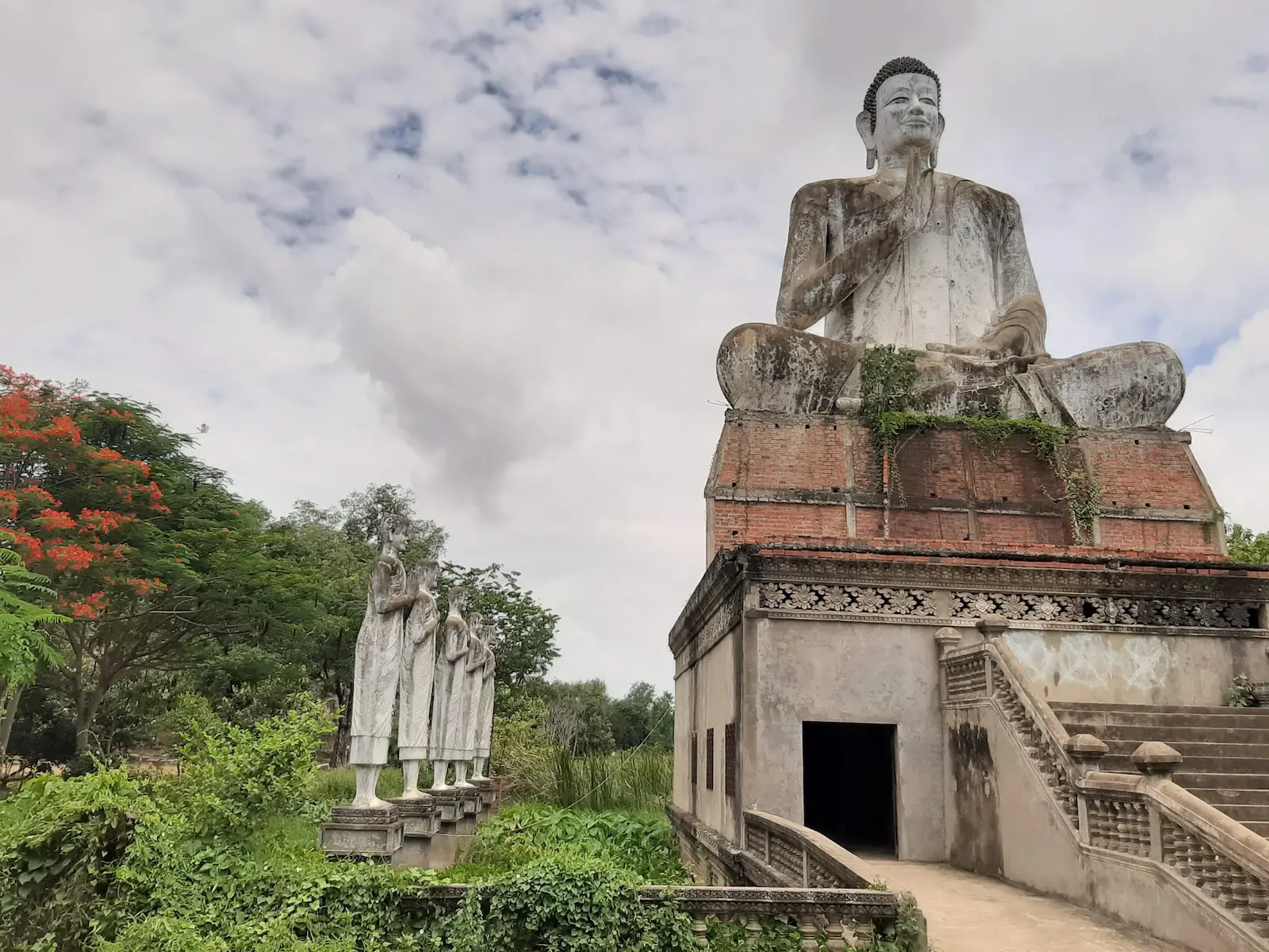 Giant Buddha statue at Ek Phnom Temple in Battambang, with statues of Buddhist monks standing in the surrounding moat.