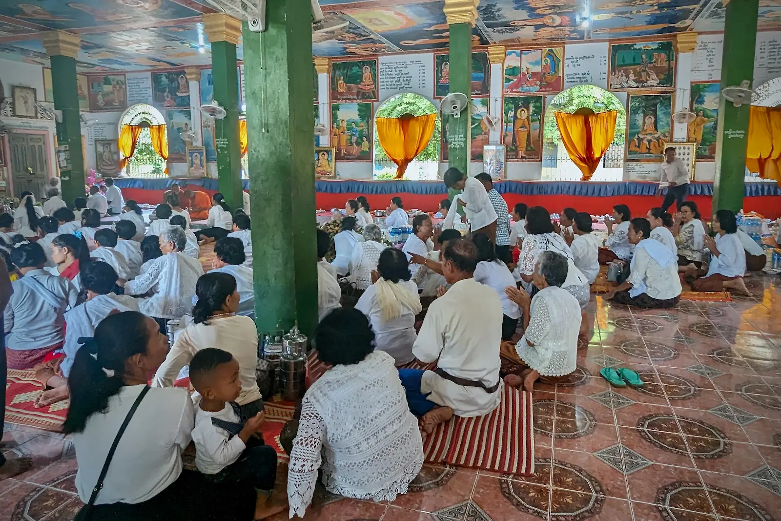 A pagoda floor is full of people wearing white sitting on the floor.