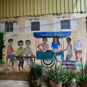 Street art on an alleyway wall of people eating at a street cart.